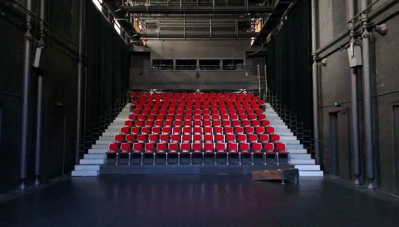 Blick von der Bühne auf leere rote Theatersessel und die technische Infrastruktur.